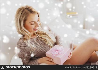 christmas, holidays and people concept - happy young woman gift box or presents in bed at home bedroom over snow. happy young woman with christmas gift in bed