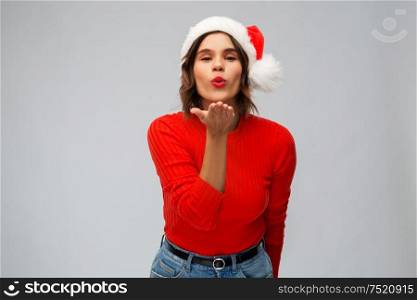 christmas, holidays and people concept - happy young woman in santa helper hat sending air kiss over grey background. happy young woman in santa hat sending air kiss