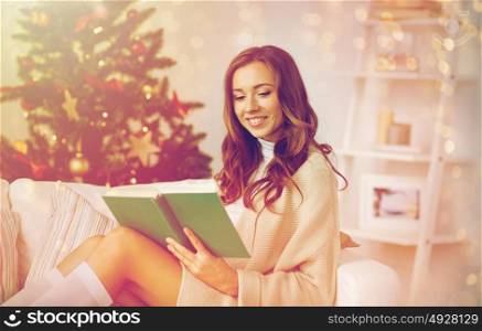 christmas, holidays and people concept - happy young woman reading book at home. happy woman reading book at home for christmas