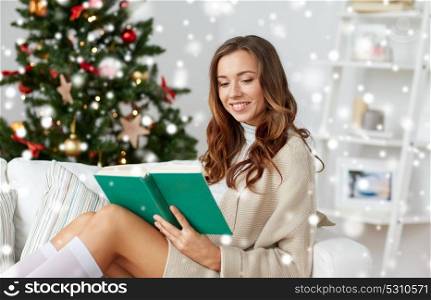 christmas, holidays and people concept - happy young woman reading book at home over snow. happy woman reading book at home for christmas