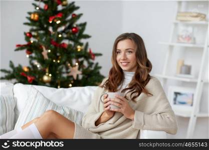 christmas, holidays and people concept - happy young woman with cup of coffee or tea at home