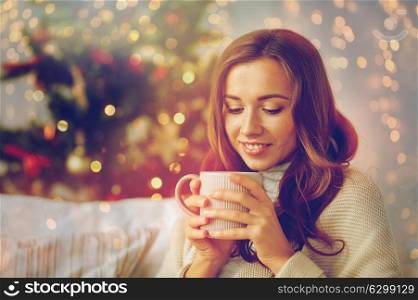 christmas, holidays and people concept - happy young woman with cup of coffee or tea at home. happy woman with cup of tea at home for christmas