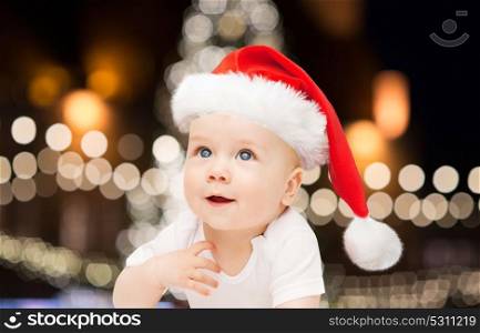 christmas, holidays and people concept - little baby boy in santa hat over lights background. little baby boy in santa hat at christmas