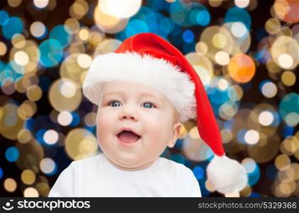 christmas, holidays and people concept - little baby boy in santa hat over lights background. little baby boy in santa hat at christmas
