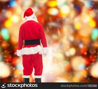 christmas, holidays and people concept - man in costume of santa claus from back over red lights background
