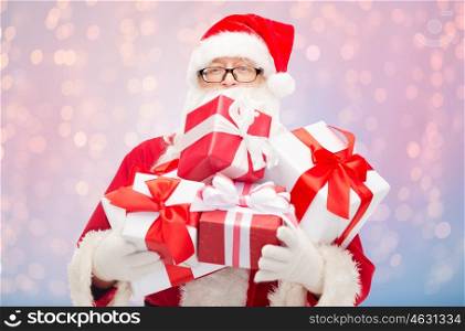 christmas, holidays and people concept - man in costume of santa claus with gift boxes over rose quartz and serenity lights background
