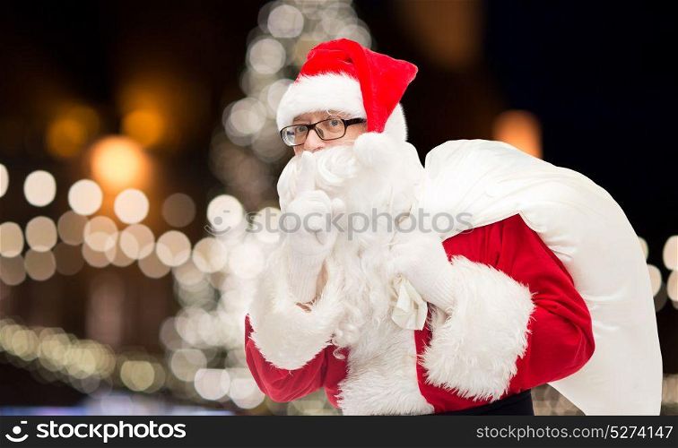 christmas, holidays and people concept - man in costume of santa claus with bag making hush gesture. man in costume of santa claus with bag