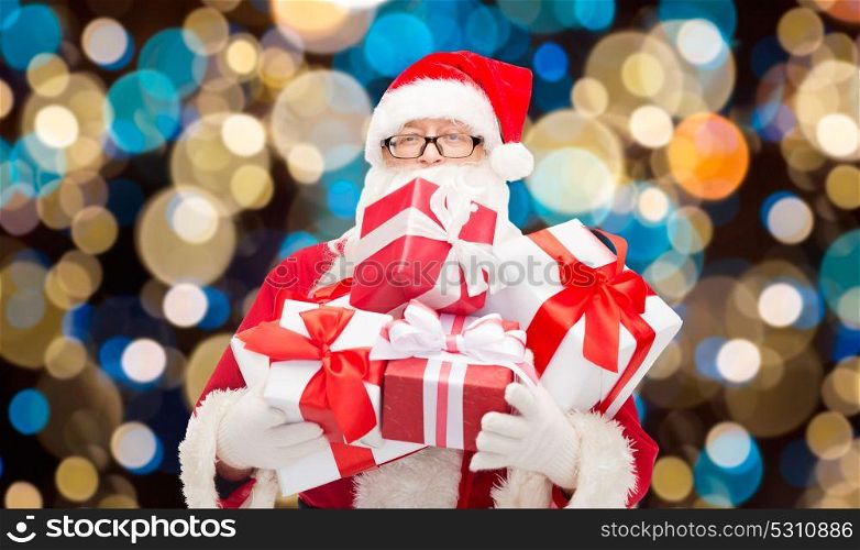 christmas, holidays and people concept - man in costume of santa claus with gift boxes over lights background. santa claus with christmas gifts over lights