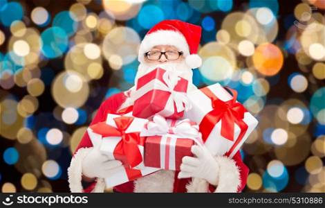 christmas, holidays and people concept - man in costume of santa claus with gift boxes over lights background. santa claus with christmas gifts over lights