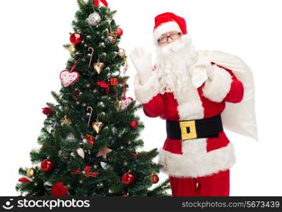 christmas, holidays and people concept - man in costume of santa claus with bag and christmas tree waving hand