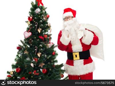 christmas, holidays and people concept - man in costume of santa claus with bag and christmas tree making hush gesture