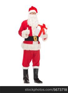 christmas, holidays and people concept - man in costume of santa claus with gift box showing thumbs up gesture
