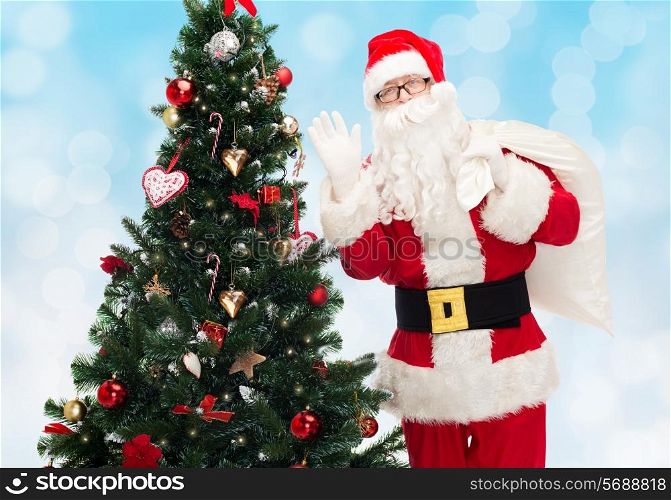 christmas, holidays and people concept - man in costume of santa claus with bag and christmas tree waving hand over blue lights background
