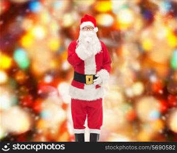 christmas, holidays and people concept - man in costume of santa claus making hush gesture over red lights background