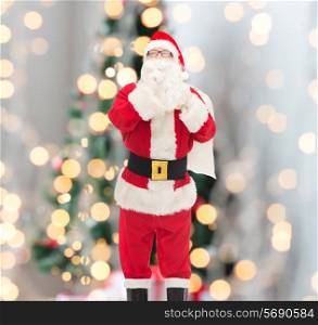 christmas, holidays and people concept - man in costume of santa claus with bag making hush gesture over tree lights background