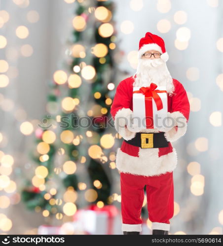 christmas, holidays and people concept - man in costume of santa claus with gift box over tree lights background