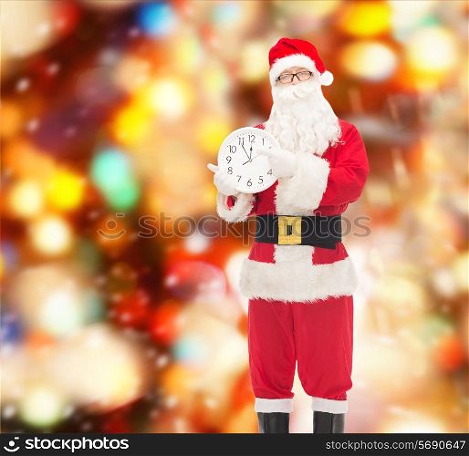 christmas, holidays and people concept - man in costume of santa claus with clock showing twelve pointing finger over red lights background