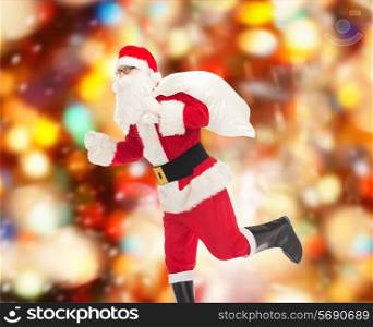 christmas, holidays and people concept - man in costume of santa claus running with bag over red lights background