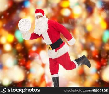 christmas, holidays and people concept - man in costume of santa claus running with clock showing twelve over red lights background