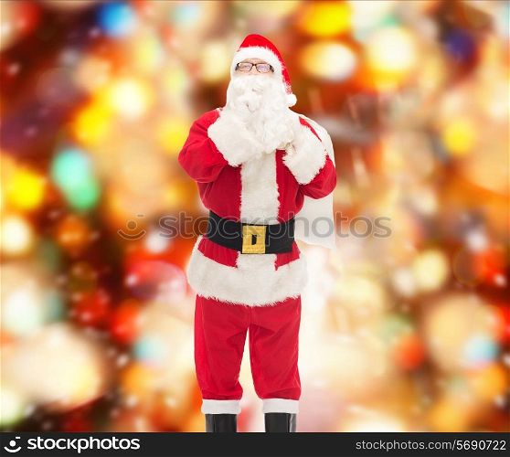 christmas, holidays and people concept - man in costume of santa claus with bag making hush gesture over red lights background