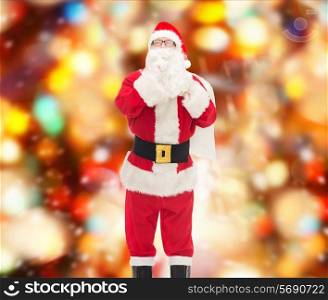 christmas, holidays and people concept - man in costume of santa claus with bag making hush gesture over red lights background