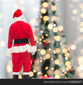 christmas, holidays and people concept - man in costume of santa claus from back over tree lights background