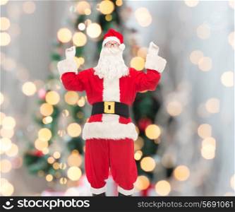 christmas, holidays and people concept - man in costume of santa claus having fun over tree lights background