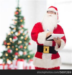christmas, holidays and people concept - man in costume of santa claus with notepad and pen over living room with tree background