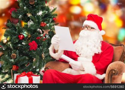 christmas, holidays and people concept - man in costume of santa claus with letter and christmas tree sitting in armchair over red lights background