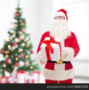 christmas, holidays and people concept - man in costume of santa claus with gift box over living room with tree