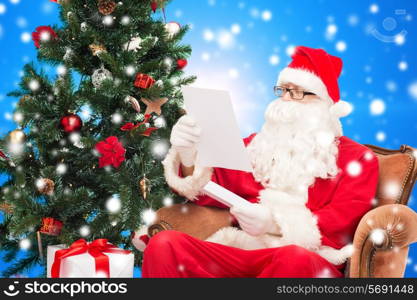 christmas, holidays and people concept - man in costume of santa claus with letter and christmas tree sitting in armchair over blue snowy background