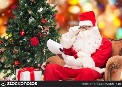 christmas, holidays and people concept - man in costume of santa claus with notepad and christmas tree sitting in armchair over red lights background