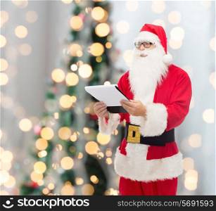christmas, holidays and people concept - man in costume of santa claus with notepad over tree lights background