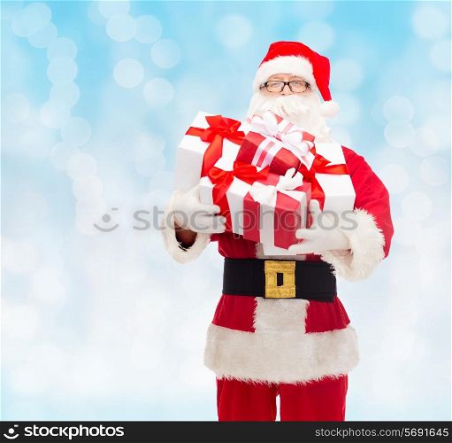 christmas, holidays and people concept - man in costume of santa claus with gift boxes over blue lights background