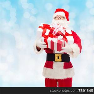 christmas, holidays and people concept - man in costume of santa claus with gift boxes over blue lights background