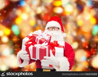 christmas, holidays and people concept - man in costume of santa claus with gift boxes over red lights background