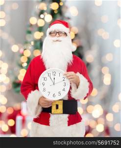 christmas, holidays and people concept - man in costume of santa claus with clock showing twelve pointing finger over tree lights background