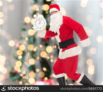 christmas, holidays and people concept - man in costume of santa claus running with clock showing twelve over tree lights background