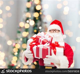 christmas, holidays and people concept - man in costume of santa claus with gift boxes over tree lights background