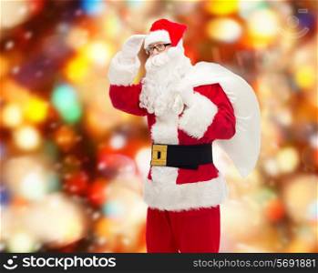 christmas, holidays and people concept - man in costume of santa claus with bag looking far away over red lights background