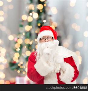 christmas, holidays and people concept - man in costume of santa claus with bag making hush gesture over tree lights background