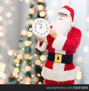 christmas, holidays and people concept - man in costume of santa claus with clock showing twelve pointing finger over tree lights background