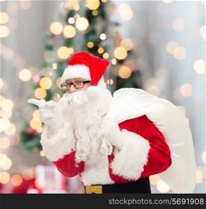 christmas, holidays and people concept - man in costume of santa claus with bag pointing finger over tree lights background