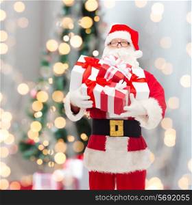 christmas, holidays and people concept - man in costume of santa claus with gift boxes over tree lights background