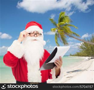 christmas, holidays and people concept - man in costume of santa claus with notepad over tropical beach background