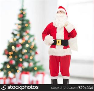 christmas, holidays and people concept - man in costume of santa claus with bag over living room and tree background