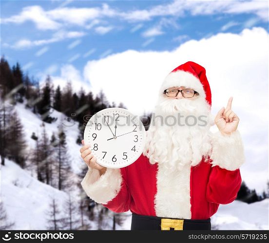 christmas, holidays and people concept - man in costume of santa claus with clock showing twelve pointing finger up over snowy mountains background