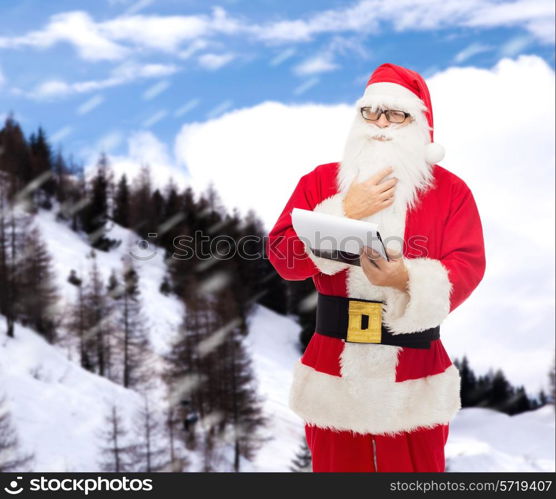 christmas, holidays and people concept - man in costume of santa claus with notepad over snowy mountains background