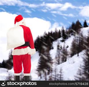 christmas, holidays and people concept - man in costume of santa claus with bag from back over snowy mountains background