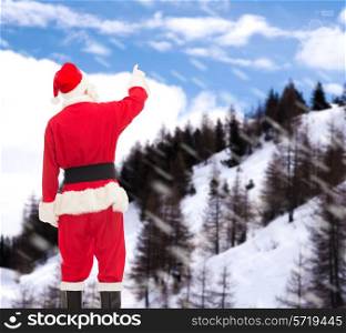 christmas, holidays and people concept - man in costume of santa claus pointing finger from back over snowy mountains background